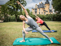 Zwei Studentinnen machen zusammen beim schönem Sonnenschein Yoga auf der Wiese im Stadtpark.