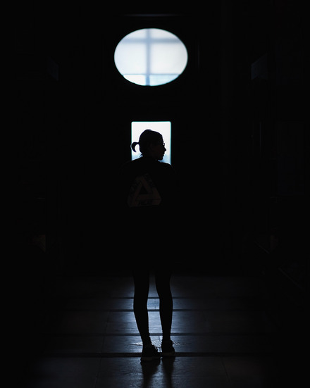 Auf dem Foto sieht man ein Oberlicht und einen ansonsten schwarzen Raum. Das Licht beleuchtet die Silhouette einer jungen Frau.