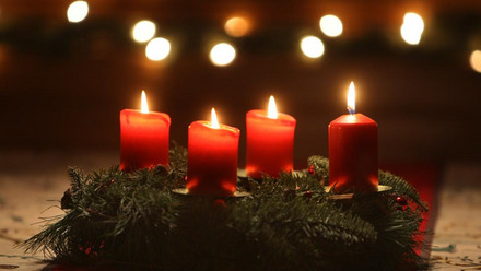 Zu sehen ist ein Adventskranz mit 4 roten, brennenden Kerzen.