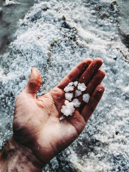 Auf dem Foto sieht man eine Hand, die Salzflocken hält. Im Hintergrund sieht man mehr Salz.