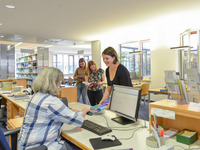 Eine Studentin leiht Bücher bei einer Mitarbeiterin aus. (Bild öffnet vergrößert)