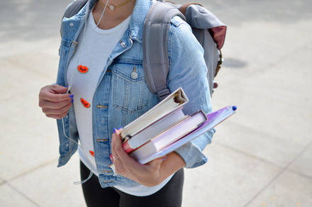 Auf dem Foto sieht man eine Studentin mit Rucksack und Büchern in der Hand.