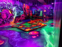 Man sieht eine in Neonfarben erstrahlenden Raum im Stil "Orks und Elfen" mit Minigolf Bahnen