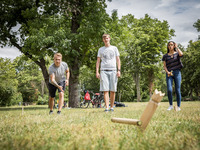 Studierende spielen Wikingerschach auf einer grünen Wiese. Sie versuchen mit einem Holzstab die Figur in der Mitte des Spielfeldes umzuwerfen.