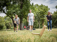 Studierende spielen Wikingerschach auf einer grünen Wiese. Sie versuchen mit einem Holzstab die Figur in der Mitte des Spielfeldes umzuwerfen. (Bild öffnet vergrößert)