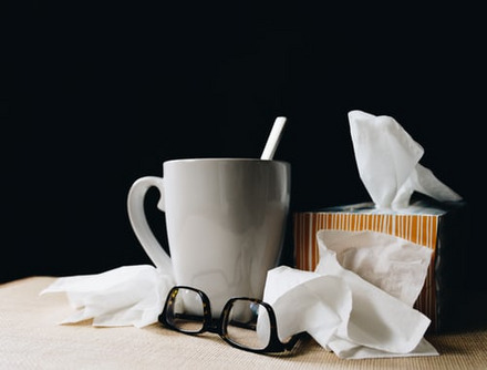 Taschentücher liegen neben einer Teetasse auf dem Tisch.