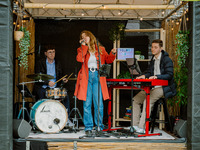 Die Bands machten Riesenstimmung auf kleinstem Raum. Auf einer kleinen Bühne spielt eine Band. Eine Person sitzt am Keyboard, eine Person spielt Gitarre und eine Person mit einem roten Mantel singt. (Bild öffnet vergrößert)