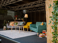 Der neue Look der Wohnzimmerbühne kam sehr gut an. Auf der Bühne stehen eine graue und eine petrolfarbene Couch, dazwischen ein gelber Sessel. Im Vordergrund steht ein flacher Tisch. Rundherum stehen viele Pflanzen, einige Bücher liegen auf dem Boden. (Bild öffnet vergrößert)