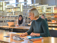 Eine Studentin sitzt am Arbeitsplatz in der Bibliothek und macht Notizen.