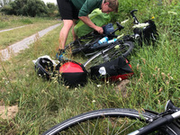 Auf dem Foto sieht man einen jungen Mann der sich über ein mit Fahrradtaschen beladenes Fahrrad beugt, dass im Gras liegt. (Bild öffnet vergrößert)