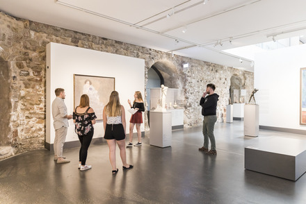 Zu sehen ist eine kleine Gruppe von Studierenden, die sich einen Vortrag von mir über das gezeigte Kunstwerk anhören.