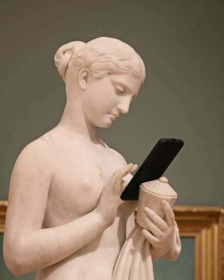 Zu sehen ist eine weibliche Statue mit einem Smartphone in der Hand. 