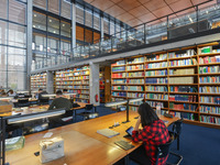 Blick auf eine große Bücherwand und einige Arbeitstische in der juristischen Bibliothek. 