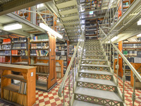 Blick auf eine schmiedeeiserne Treppe, kunstvoll angeordnete Bodenfliesen und jede Menge Bücherregale im Magazin.