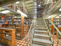 Blick auf eine schmiedeeiserne Treppe, kunstvoll angeordnete Bodenfliesen und jede Menge Bücherregale im Magazin. (Bild öffnet vergrößert)