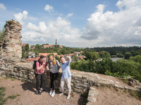 Studierende machen ein Selfie vor alten Mauern, dahinter sieht man die Saale und das Giebichensteinviertel.