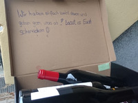 Ein Schuhkarton mit einladender Aufschrift und voller Rotweinflaschen am Gehwegrand