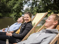 Junge Menschen genießen die Sonne und chillen im Liegestuhl am Saaleufer.