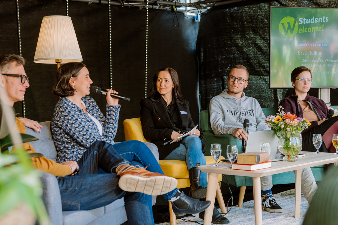 Mehrere Menschen sitzen in gemütlicher Atmosphäre an einen Tisch und sprechen miteinander.