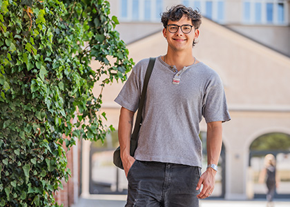 Philipp steht auf dem Steintor Campus zwischen den Bäumen vor der Bibliothek